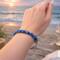 Blue seed bead Kumihimo bracelet on wrist by the ocean, handmade glass bead bracelet inspired by coastal colors